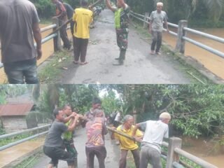 Babinsa Koramil 09/Samatiga Sertu Heru Santoso Bersama Warga Desa Leukeun Bergotong Royong Membersihkan Tumpukan Sampah dan Kayu Besar yang Menyumbat Aliran Sungai di Jembatan Utama